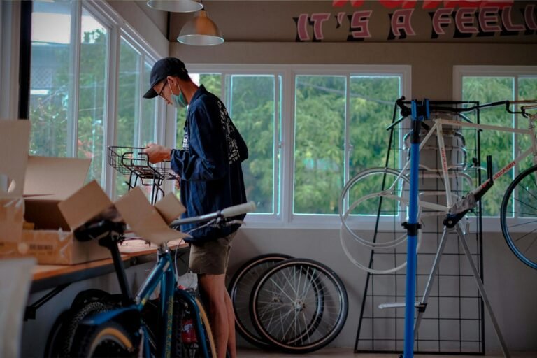A man working on a bicycle assembly in a bright indoor workshop setting.